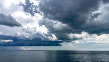 Obraz premium A dark, dramatic sky filled with heavy, ominous clouds looms over a calm ocean surface. A rain shower descends in the distance