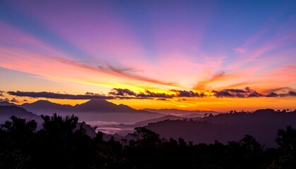 Fototapeta premium A breathtaking sunset illuminates layered mountain ranges, with vibrant sky and silhouette trees in foreground