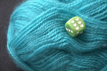A green die showing six placed on a ball of green yarn, close-up with copy space. Symbol of life’s thread, luck, fate, chance, and free will.