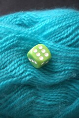 A green die showing six placed on a ball of green yarn, close-up with copy space. Symbol of...