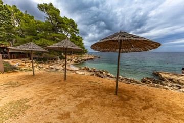 Tara Beach, Rab, sun umbrellas on the shore of the Adriatic Sea, cloudy, threatening sky, azure water