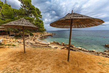 Tara Beach, Rab, sun umbrellas on the shore of the Adriatic Sea, cloudy, threatening sky, azure water