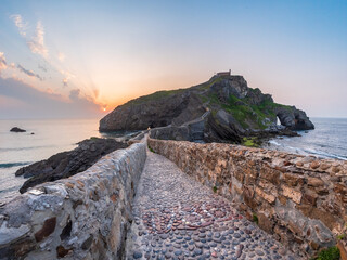 Ancient stone bridge leading to Gaztelugatxe islet at sunset Basque Country Spain symbol of journey solitude spirituality dramatic seascape inspiration