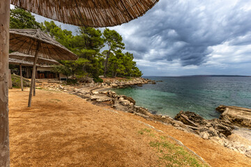 Tara Beach, Rab, sun umbrellas on the shore of the Adriatic Sea, cloudy, threatening sky, azure water