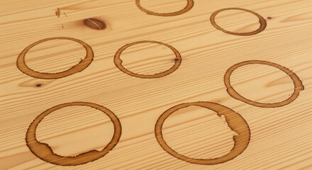 A Top View of Multiple Coffee Stains on Wood. A bright, high-angle shot of a light-colored wooden table with multiple, messy coffee rings scattered across the surface