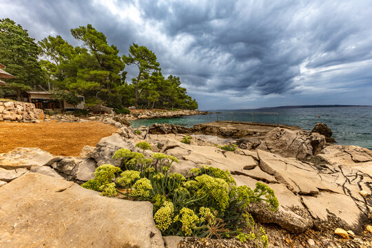 Tara Beach, Rab, sun umbrellas on the shore of the Adriatic Sea, cloudy, threatening sky, azure water