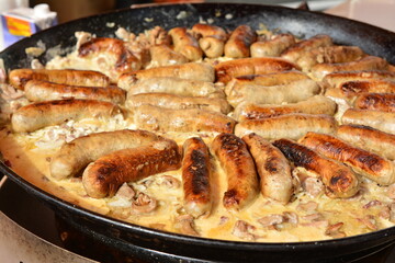 Fried sausages with mushrooms in a large frying pan on the market