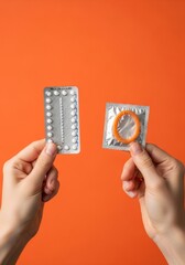Woman hand holding oral contraceptive pill blister pack and a condom for safe sex promotion on orange backdrop. Birth control method choice. Vertical poster template with copyspace. 