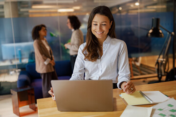 A professional woman is deeply engaged with her laptop, highlighting a dynamic and collaborative office atmosphere