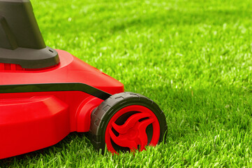 A red and black lawn mower stands on the lawn.