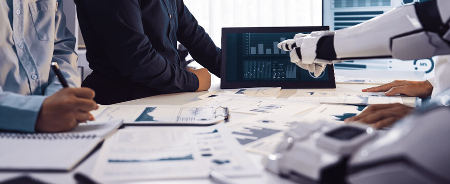 A business team engages in a meeting featuring artificial intelligence technology. Interactive charts and graphs are displayed, showcasing data analysis in a modern office setting.Noogenesis