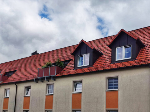 Red tile roof of residential building with attic against blue sky with dense clouds. European architecture. Close-up. Copy space. Selective focus. - Powered by Adobe
