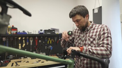Bicycle mechanic wraps bicycle tape around handlebars of gravel bicycle at his workstation in cycle repair shop. Cycle engineer winding bike handlebar tape on gravel bike at job site in workshop.