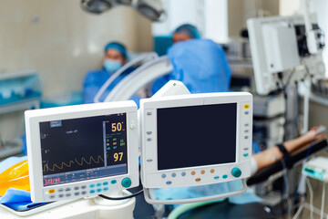 Surgical monitors display vital signs in a hospital setting. Monitors track vital signs during a surgical procedure in a modern hospital operating room with medical staff present.