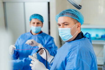 Medical team performs procedure in sterile environment. Two healthcare professionals in masks and...