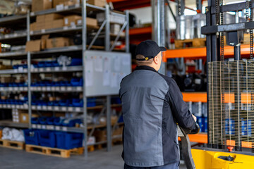 Warehouse worker with forklift in industrial area. A worker in a black cap navigates a forklift in a busy warehouse full of supplies and equipment.