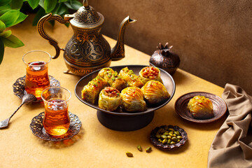 Baklava dessert on a stand served with tea in armudu glass from a copper teapot. Yellow and brown background. Close up.