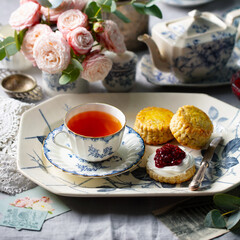 Scone with jam, clotted cream and cup of tea. Rose flower background. Close up.