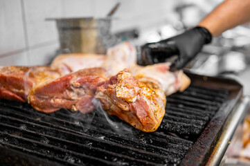 Grilled seasoned meat on a commercial barbecue grill, with smoke rising and a gloved hand adjusting the cuts in a professional kitchen setting