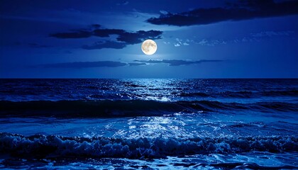 A full, bright moon illuminates dark, churning ocean waves under a deep blue, cloud-streaked sky, reflecting light on the water