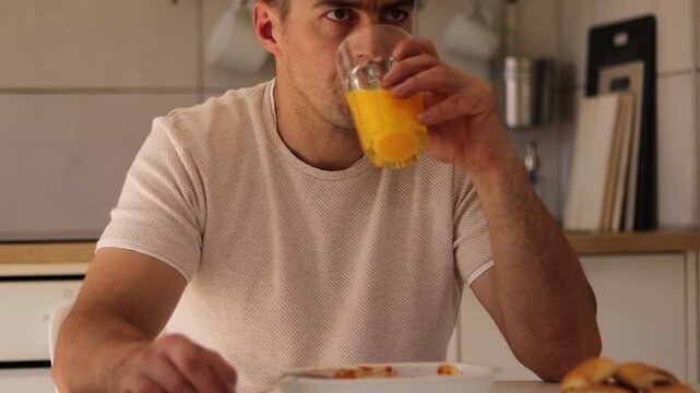 In a comfortable kitchen setting, a man savors a plate of lasagne while holding a glass of orange juice. He appears to enjoy this homemade meal during lunch