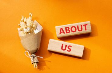 About us symbol. Concept word About us on wooden blocks. Beautiful orange background with bouquet...