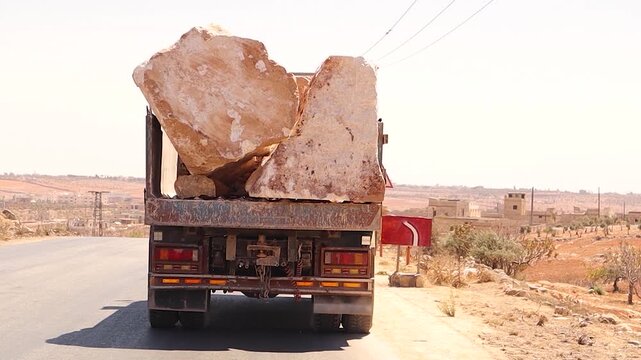 Truck loaded with huge stones driving on a rural road without safety measures, highlighting the danger of falling rocks and unsafe transport. Ideal for documentaries and road safety reports.