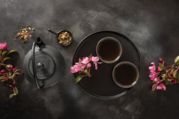 Black cast iron teapot and cups with asian tea and cherry blossom on black table. Composition with...