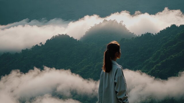 Woman standing in the middle of mountain range. A woman observing the fog in mountains. A peaceful landscape of nature. A woman positioned at the center of a mountain range lifestyle. - Powered by Adobe