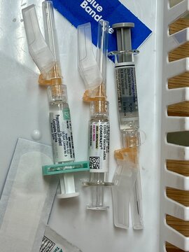 A plastic mesh tray basket with vaccine syringes for Covid, flu and pneumonia and blue bandages