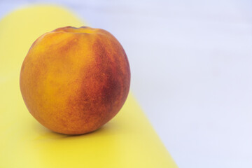 Single fresh ripe peach fruit on colorful yellow and white background, organic summer food closeup for healthy eating and nutrition
