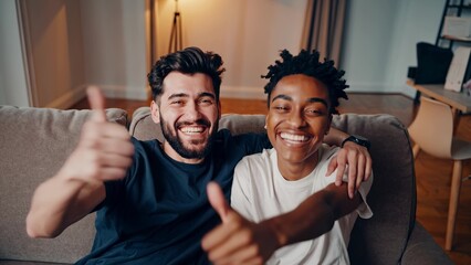 Two men sitting on couch giving thumbs up. Friends are setting up couch for casual setting. Man living in a room with a relaxed mood. Two men on a sofa giving a thumbs-up lifestyle.