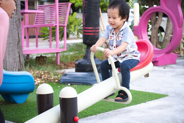 Portrait of a 2-3 year old little boy and his mother happily playing with a seesaw in the playground. Happy family time.