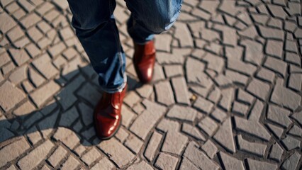 A man in blue jeans and red shoes. Man walking in leather shoes. A pair of casual jeans on a cobblestone in the city. A person wearing blue jeans and red footwear lifestyle.