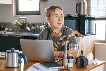  Gen Z woman working from home at cozy kitchen table with laptop and phone. Digital nomad lifestyle, mindfulness, remote work, balance, mental calm and modern freelancing