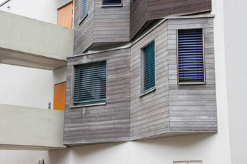 Modern architectural design featuring wooden exterior and blue window shutters, showcasing unique angles and textures in a contemporary urban setting with clean lines
