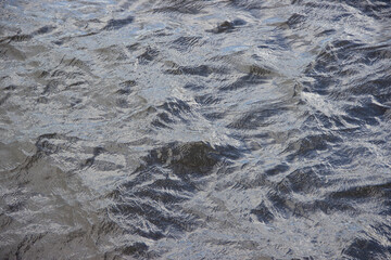 Textured surface of rippling water reflecting light, creating a dynamic interplay of shadows and highlights, showcasing the beauty of natural aquatic environments