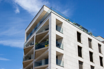 Modern residential building with sleek architecture, featuring balconies adorned with greenery, set against a bright blue sky, showcasing contemporary urban living