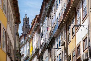 A narrow alleyway on a sloping street in Porto, lined with typical houses with balconies and colorful paint, with the Clerigos Tower in the background