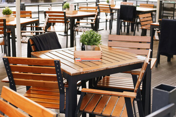 Outdoor cafe with wooden tables. Chairs arranged in row. Potted plants decoration. Terrace seating area. Empty restaurant before guests. Modern lifestyle dining concept. Social urban leisure place.