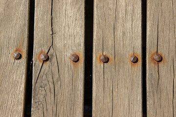 Weathered wooden planks with visible grain and rusted bolts create a rustic surface texture,...