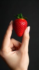 Obraz premium Hand holding a bright red strawberry