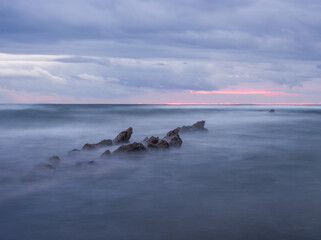 Misty seascape at a rocky beach in the Basque Country - A long exposure of the ocean smoothing over jagged rocks, with a soft horizon under a cloudy sky.