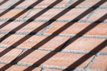 Diagonal shadows falling over a red brick wall in daylight, creating a striking geometric composition