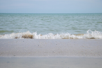 Small sea wave breaking on sandy beach shore with blue horizon and calm ocean water during summer...