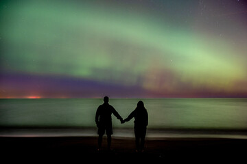 silhouette of man and woman at night looking at northern lights