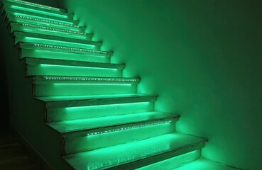 Sleek staircase steps illuminated by gentle green LED strip lights, creating fresh, modern ambience in minimalist apartment interior. Light spills from under step, visible from high vantage point.