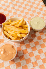 French fries with sauces around them on a checkered tablecloth.