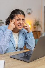 Tired ill Indian woman suffering from headache problem tension and migraine stress at home office desk workplace. Pretty freelancer broker worker girl works on laptop netbook. Overworking. Vertical.
