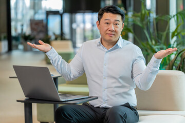 What. Why. Angry Chinese businessman raising hands in indignant expression, asking reason of failure, demonstrating disbelief irritation by troubles. Guy manager in shirt sitting in office lobby.